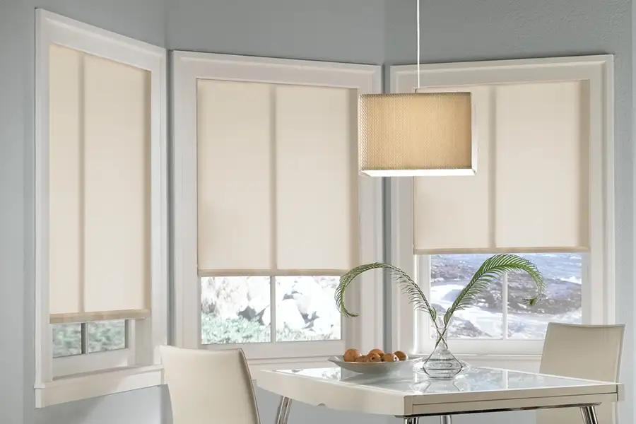 Colorful or neutral? Roller shades give you many color options for decorating your bay window. Beige roller shades on a bay window in a kitchen nook