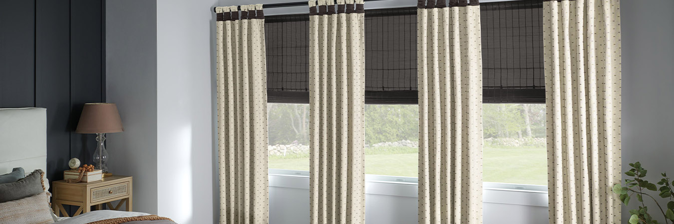 Cream curtains paired with gray natural window shades in a bedroom