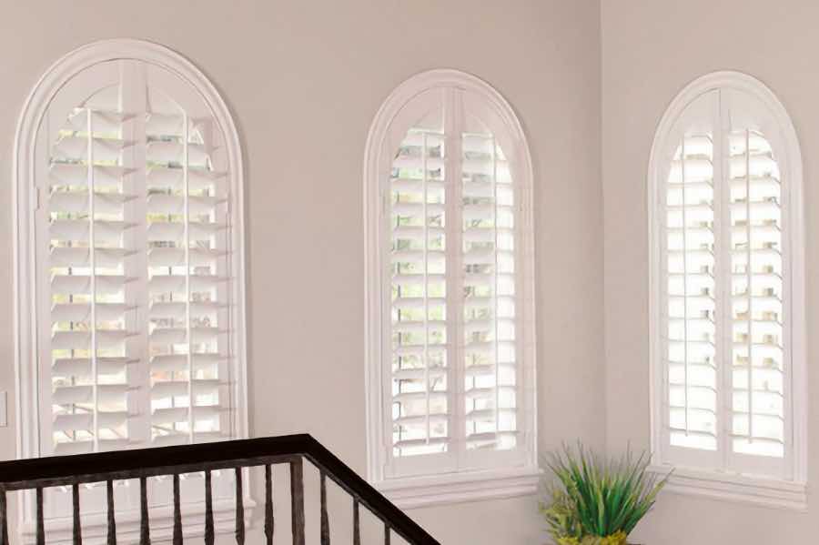White plantation shutters on arched windows in a stairwell