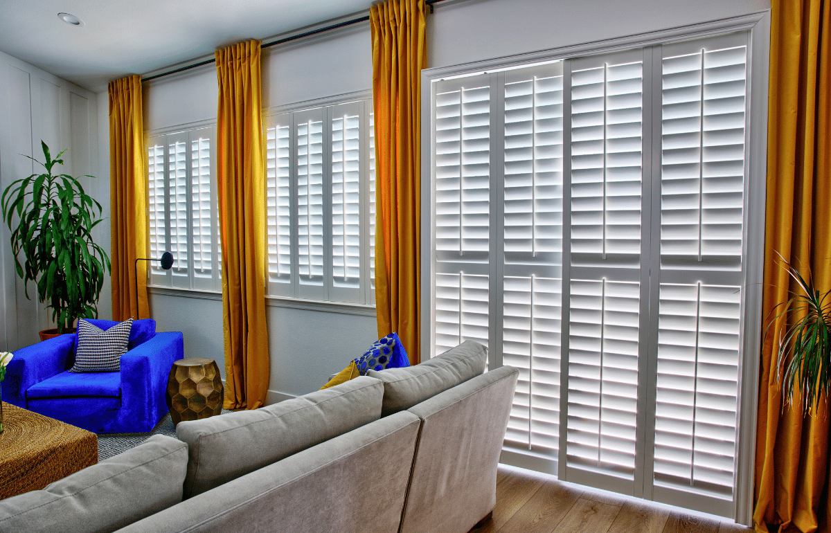 White polywood shutters accentuated by gold curtains in a white living room