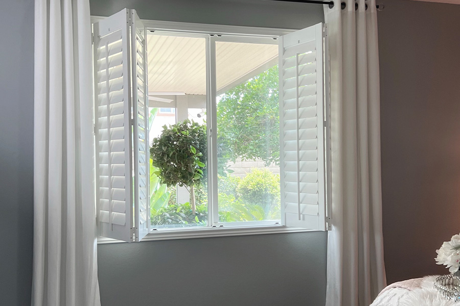 Folded and opened white Plantation shutters within a bedroom window.