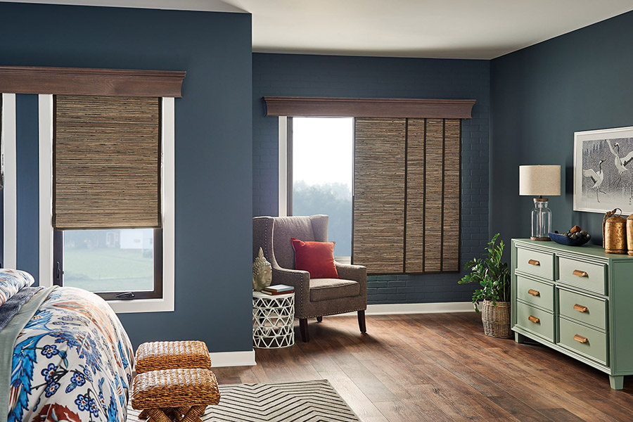 Woven fiber window shades on windows in a teal bedroom with an accent chair, side table, stools, and green dresser