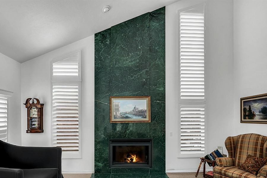 Unique raked and angled windows need a unique window treatment like lovely interior shutters. White Polywood shutters on angled windows on each side of a living room fireplace