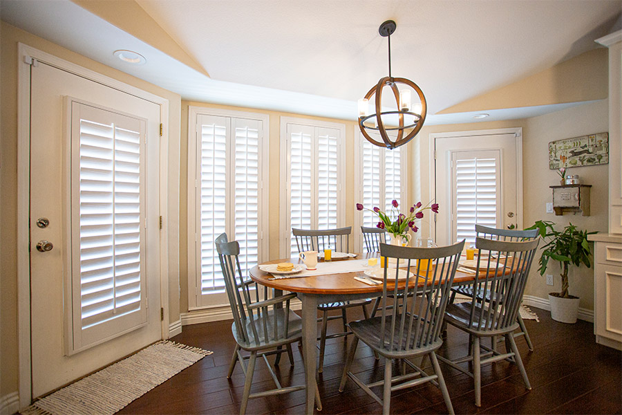 White Polywood shutters on doors and tall windows within a breakfast nook.