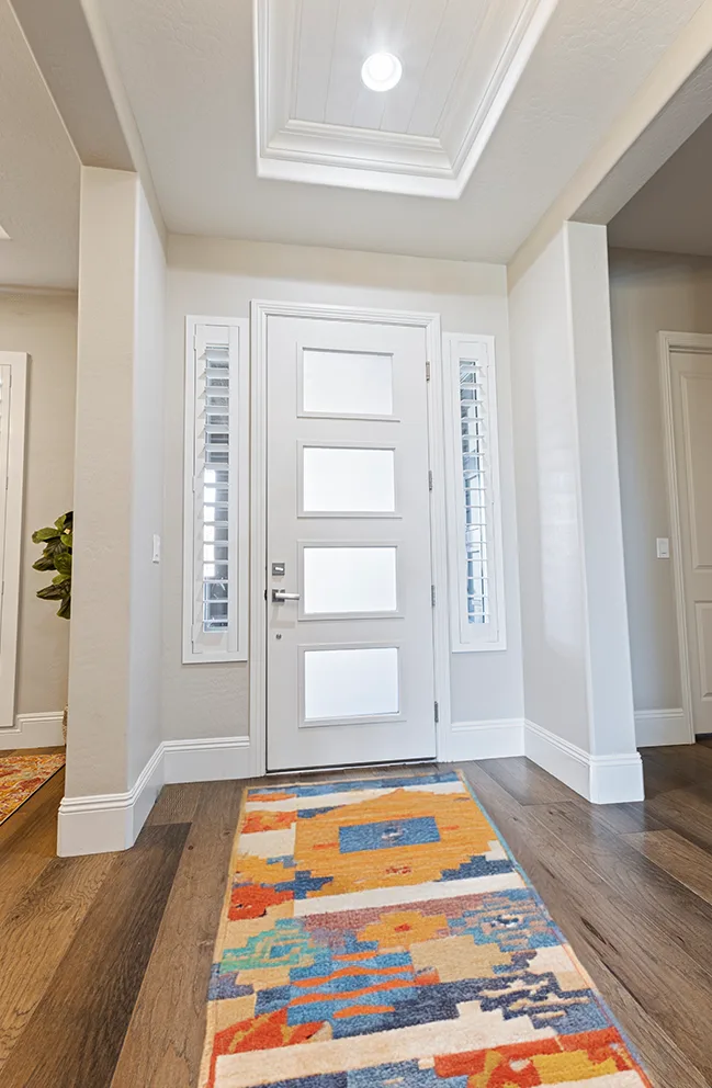 Sidelights with white shutters in a white and beige entryway with wooden flooring