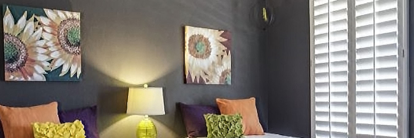 Colorful bedroom with two twin beds next to white polywood shutters.