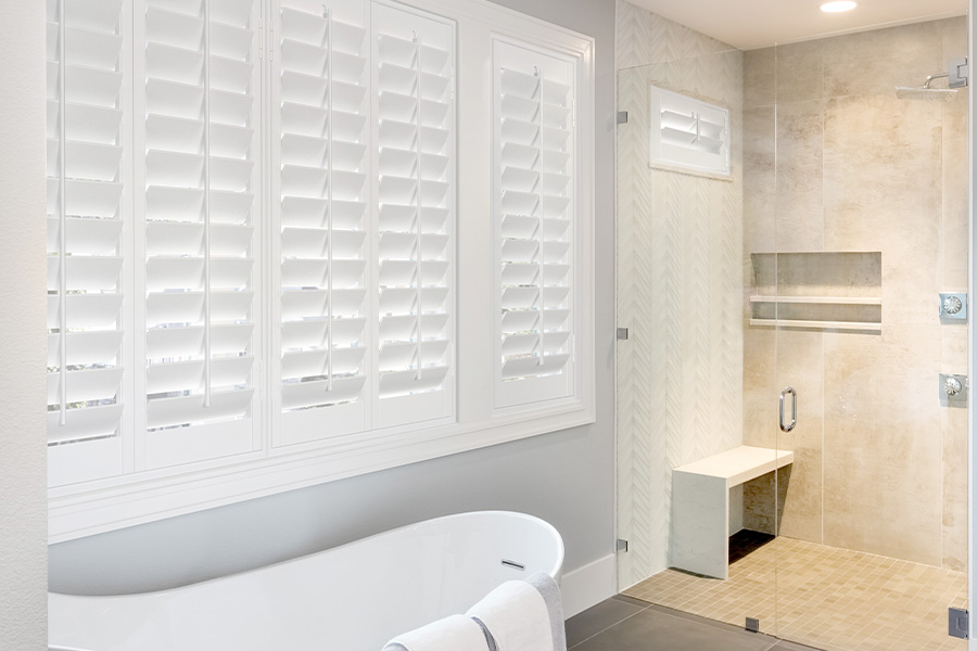 Polywood shutters on a large window above a bathtub and on a small window in a shower