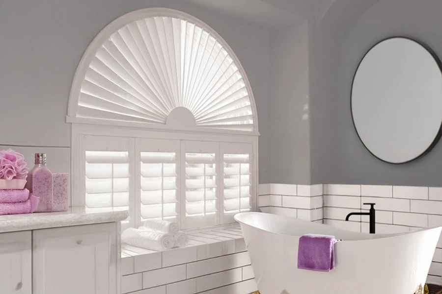 Only interior shutters show off the beauty of an arched window while still letting you block sunlight. White Polywood shutters and sunburst shutter on an arched bathroom window