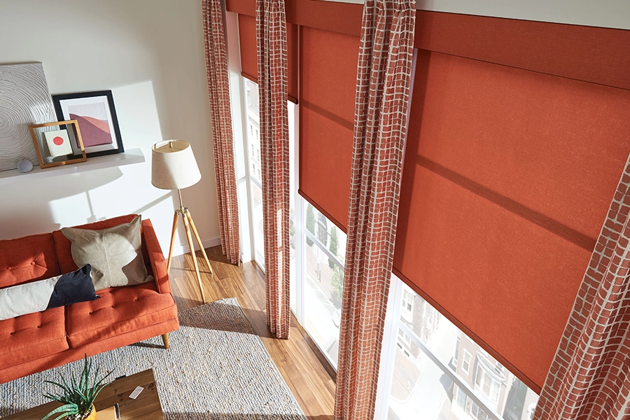 Layered window treatments can look incredible when you use matching colors for a harmonious look. Orange window shades paired with orange patterned drapes on living room windows